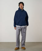 Model wearing a natural dyed grey Gramicci Gadget Pants and blue jacket on a light-tone background.
