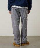 Back view of a model wearing a Gramicci natural dyed grey Gadget Pants against a light-tone background.
