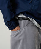 Model wearing a Gramicci natural dyed grey Gadget Pants with visible branding against a light-tone background.
