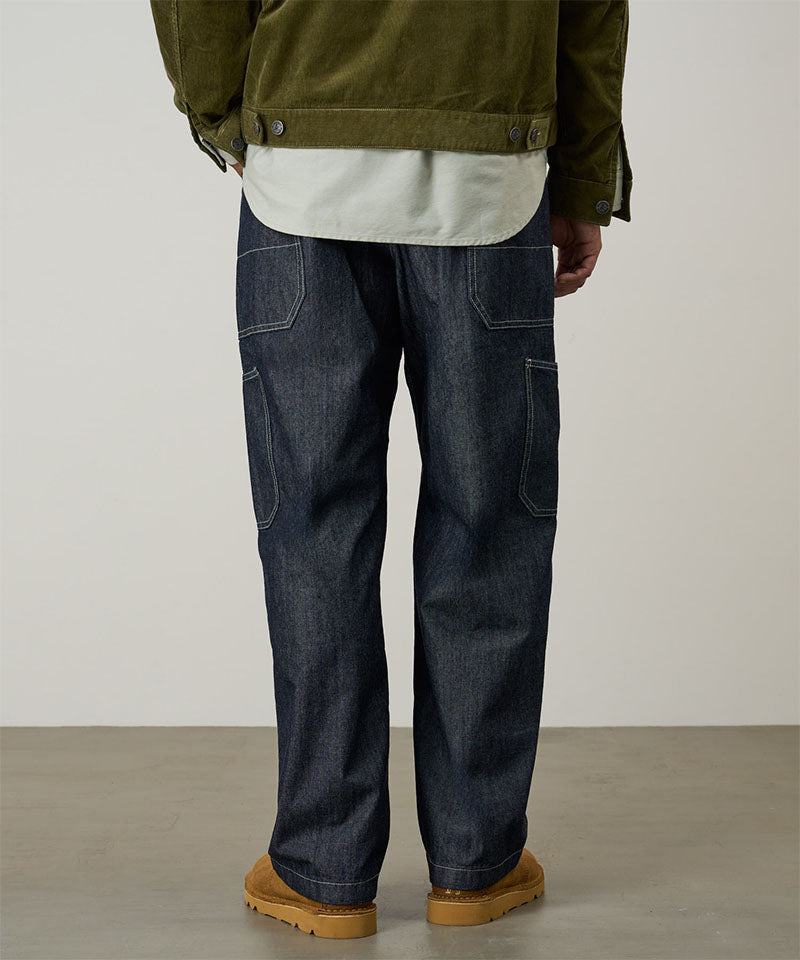 Back view of a model wearing navy Japanese Chambray Rock Slide Pant and a moss green jacket on a light-tone background.