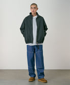 Model wearing the Gramicci Japanese Chambray Double Knee pant in blue and a dark green jacket on a light tone background.

