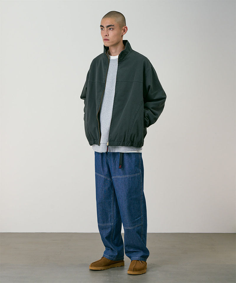 Model wearing the Gramicci Japanese Chambray Double Knee pant in blue and a dark green jacket on a light tone background.
