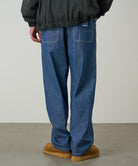 Rear view of a model wearing the Gramicci Japanese Chambray Double Knee pant in blue on a light tone background.
