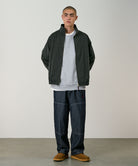 Model wearing the Gramicci Japanese Chambray Double Knee pant in navy and a dark green jacket on a light tone background.

