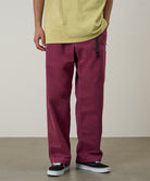 Model wearing burgundy Gramicci Milton Pants and a lime green shirt on a light-tone background.