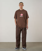 Model wearing walnut Gramicci Milton Pants and a brown shirt on a light-tone background.