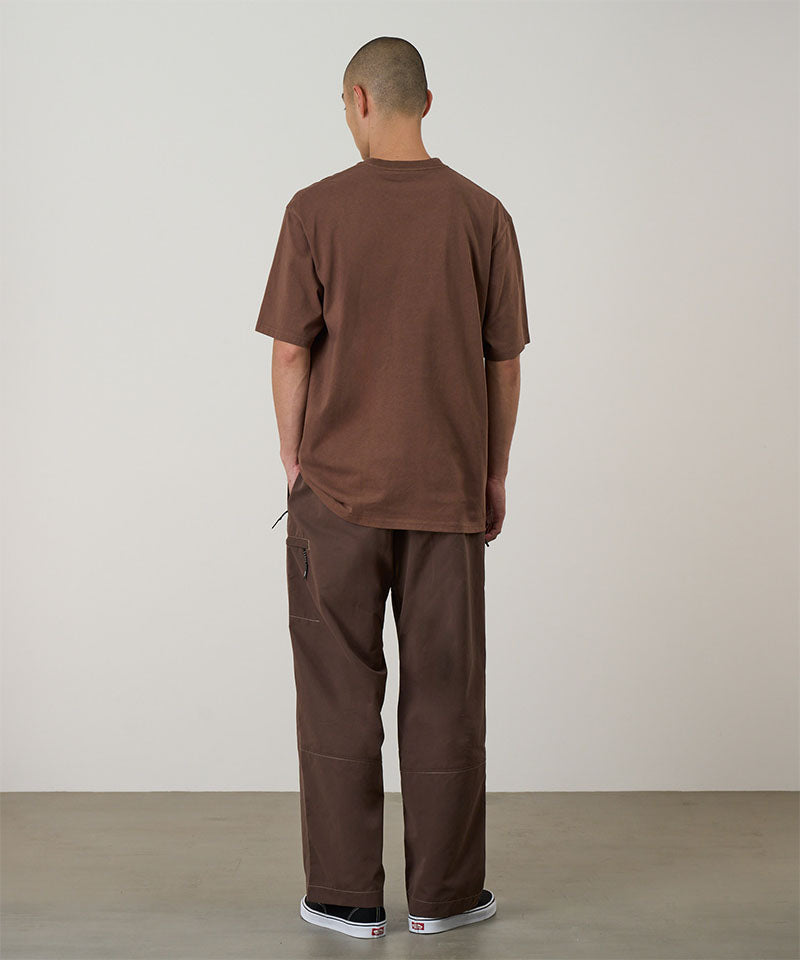 Back view of a model wearing walnut Gramicci Milton Pants and a brown shirt on a light-tone background.