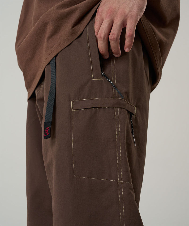 Model wearing walnut Gramicci Milton Pants and a brown shirt on a light-tone background.