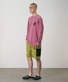 Person wearing a red  long-sleeve shirt and green shorts against a plain background