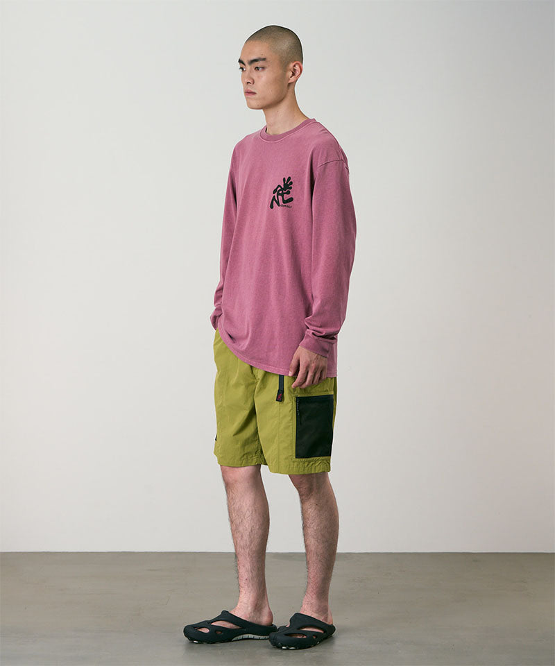 Person wearing a red  long-sleeve shirt and green shorts against a plain background