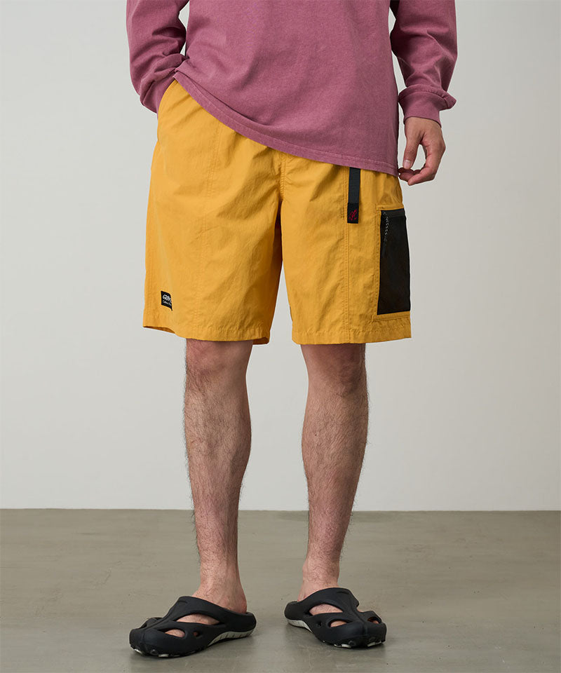 Person wearing yellow shorts with a black patch and a red long-sleeve shirt on a plain background