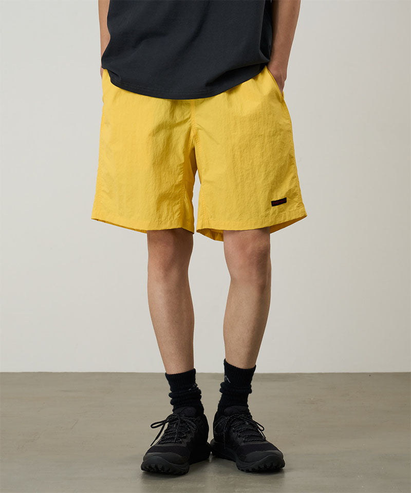 Person wearing yellow shorts and black shoes on a plain background