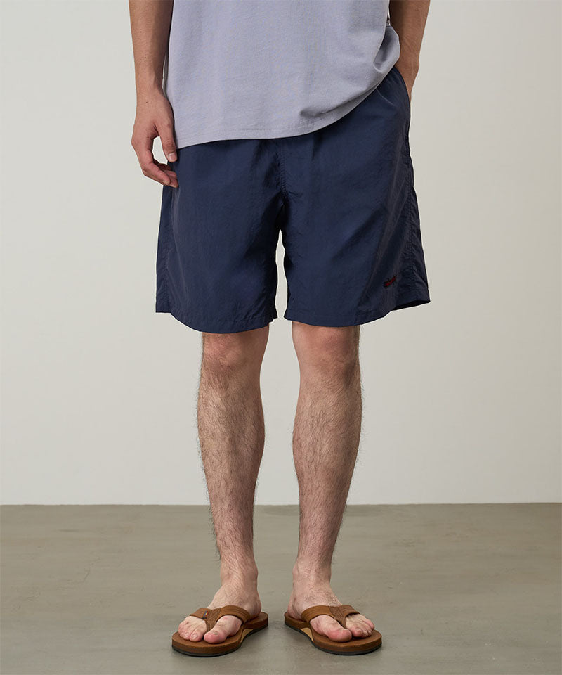 Person wearing navy shorts and a light gray shirt on a plain background