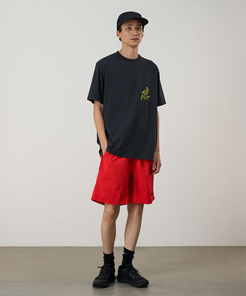 Person wearing a black t-shirt with a logo and red shorts against a plain background