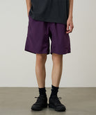 Person wearing purple shorts and black shoes on a plain background