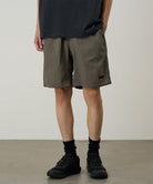 Person wearing olive green shorts and black shoes on a plain background