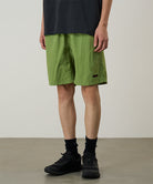 Person wearing green shorts and black shoes on a plain background