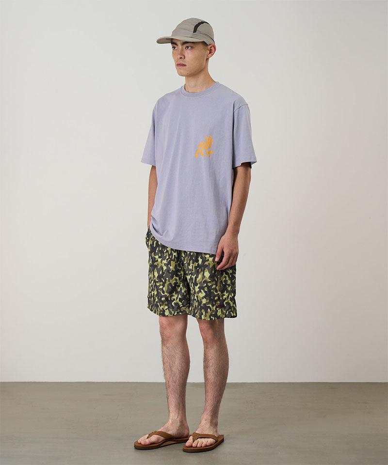 Person wearing a light purple t-shirt with a logo and camouflage shorts on a plain background