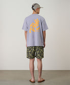 Person wearing a light gray t-shirt with a yellow graphic and camouflage shorts on a plain background