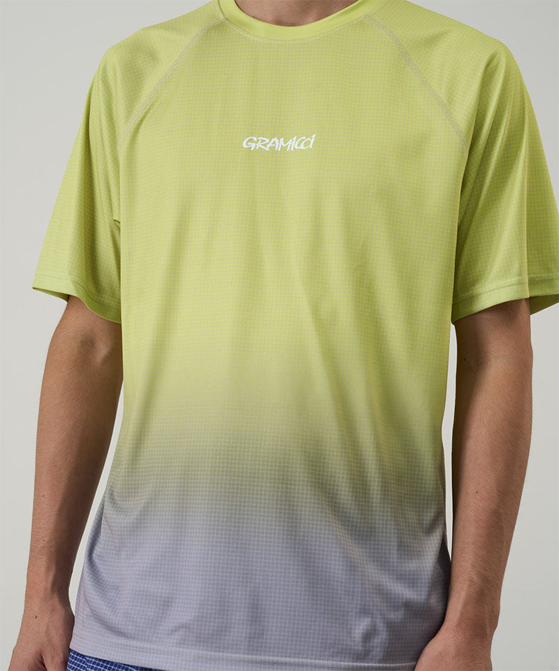 Model wearing a Gramicci yellow gradient UPF Shield S/S Top with a white Gramicci graphic against a light-tone background.
