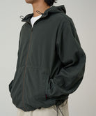 Side view of a model wearing the Gramicci Beach Hoodie Jacket in shadow, highlighting the adjustable hood drawstrings and pocket detail on a light tone background.