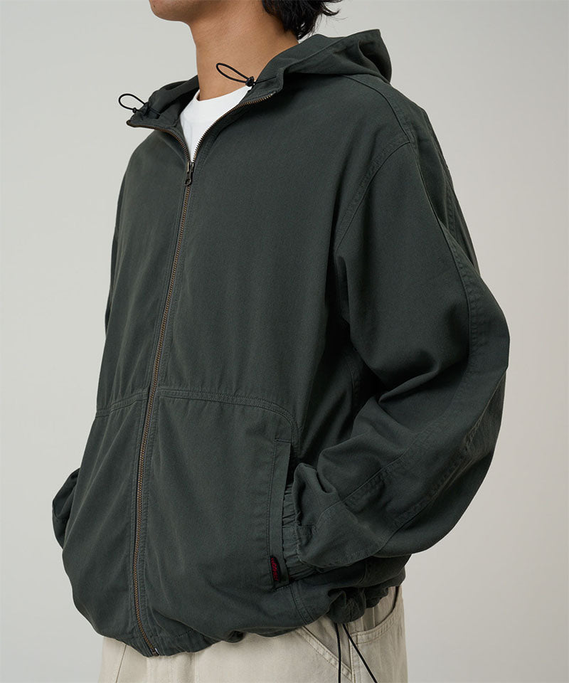 Side view of a model wearing the Gramicci Beach Hoodie Jacket in shadow, highlighting the adjustable hood drawstrings and pocket detail on a light tone background.