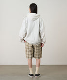 Back view of a model wearing the Gramicci Beach Hoodie Jacket in stone with tan plaid shorts on a light tone background.
