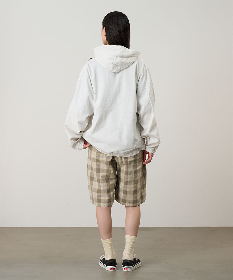 Back view of a model wearing the Gramicci Beach Hoodie Jacket in stone with tan plaid shorts on a light tone background.