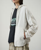 Side view of a model wearing the Gramicci Beach Hoodie Jacket in stone, highlighting the adjustable hood drawstrings and pocket detail on a light tone background.