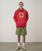 Person wearing a red hoodie with a sunflower design and plaid shorts on a plain background