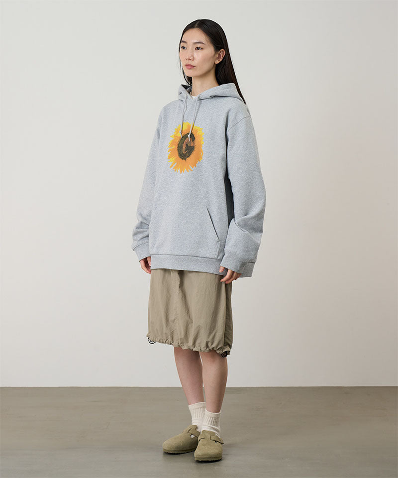 Person wearing a gray hoodie with a sunflower design, beige shorts, and green shoes on a plain background