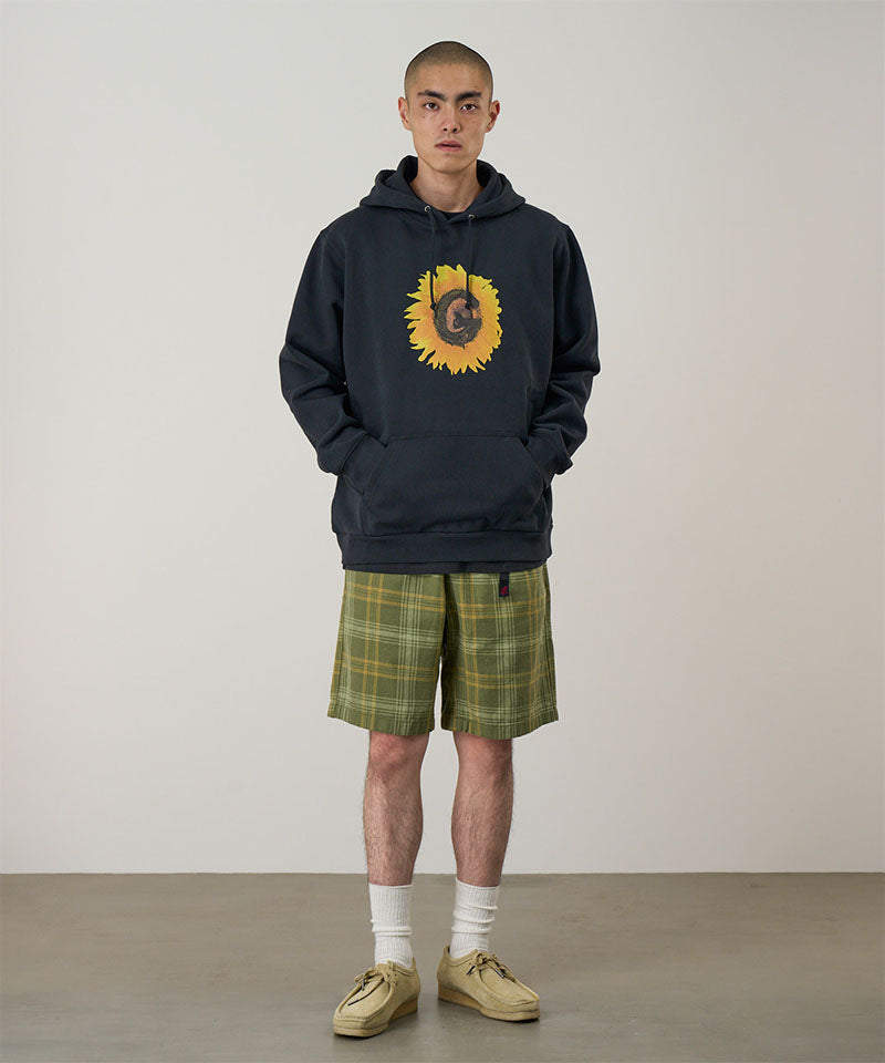 Person wearing a dark hoodie with a sunflower design and plaid shorts on a plain background