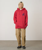 Person wearing a red hoodie with a logo and beige pants on a plain background