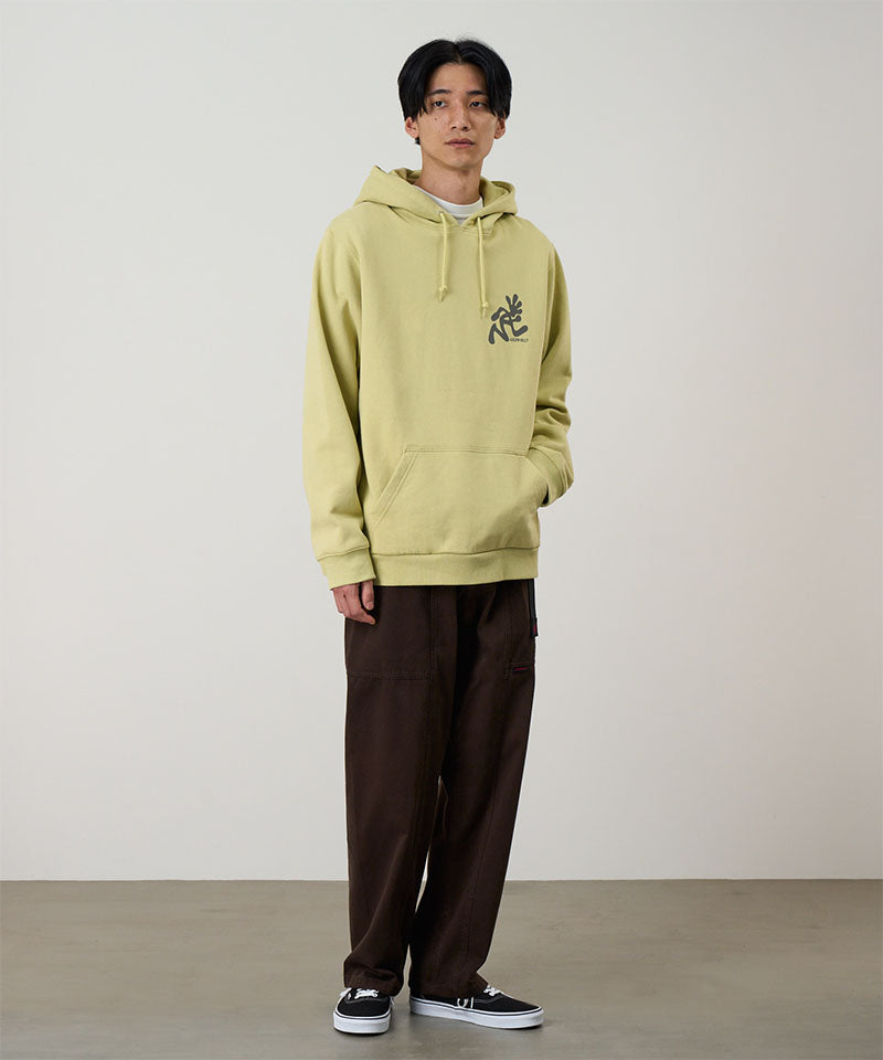 Person wearing a light green hoodie with a logo and brown pants on a plain background