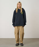 Person wearing a black hoodie with a logo and beige pants on a plain background