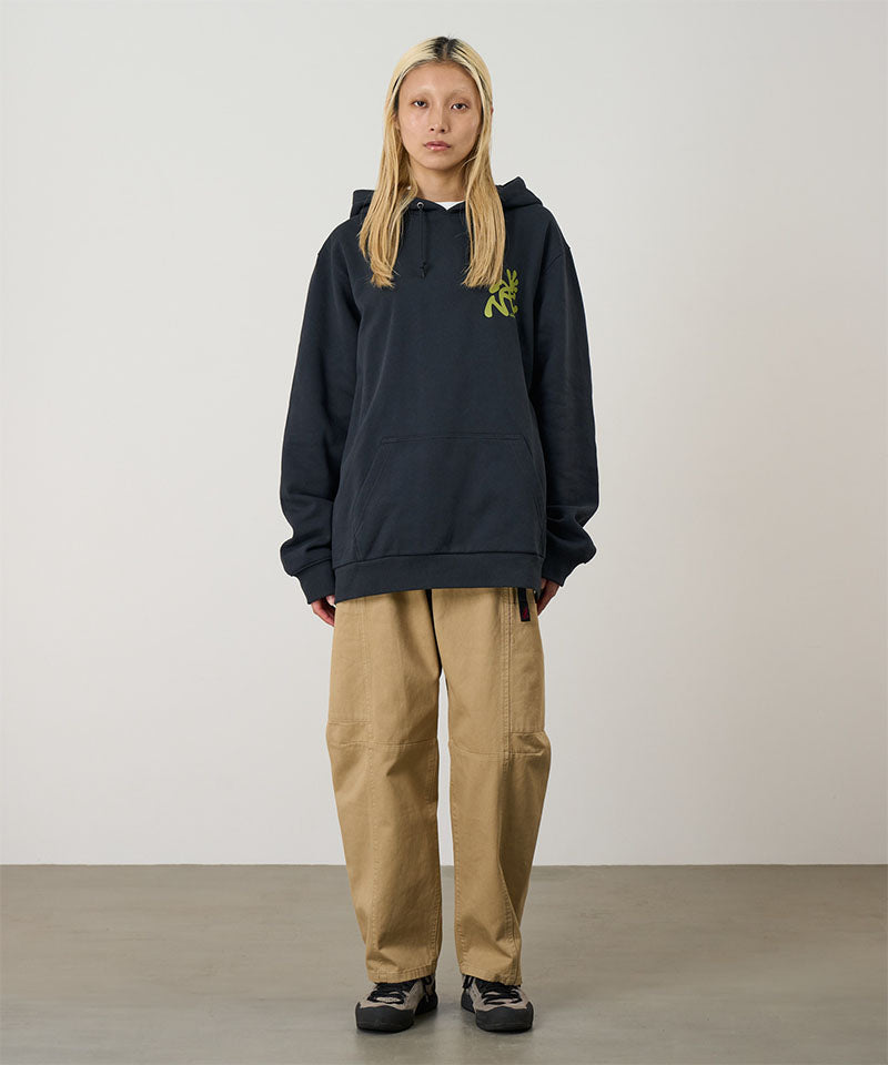 Person wearing a black hoodie with a logo and beige pants on a plain background