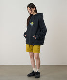 Person wearing a black hoodie with a graphic design and yellow shorts on a plain background