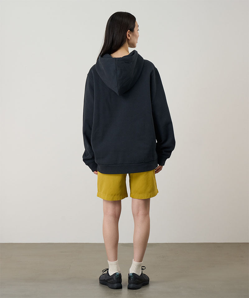 Person wearing a black hoodie and yellow shorts standing against a plain background