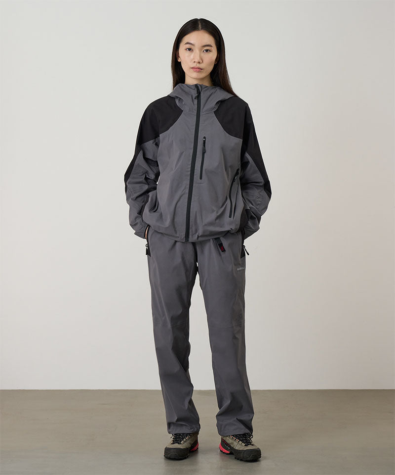 Person wearing a gray raincoat and pants on a light tone background