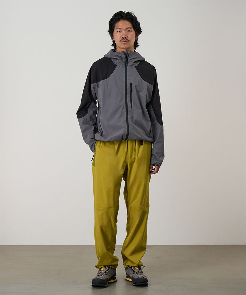 Person wearing a gray and black jacket with olive yellow pants on a light tone background