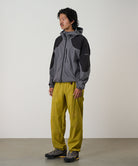 Person wearing a gray and black jacket with yellow olive pants on a light tone background