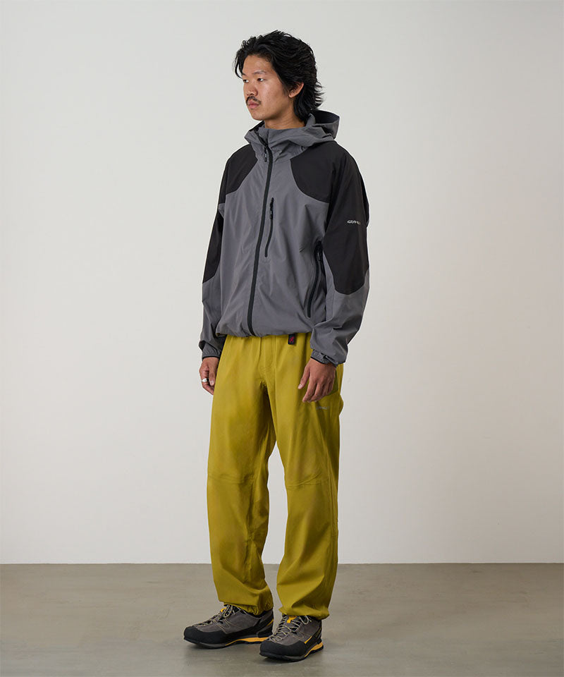 Person wearing a gray and black jacket with yellow olive pants on a light tone background