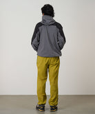 Person wearing a gray and black jacket with yellow pants against a light tone background