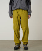 Person wearing mustard yellow pants and a gray jacket on a light tone background