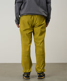 Person wearing yellow olive pants and a gray jacket on a light tone background