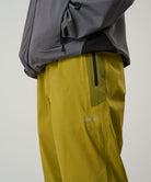 Person wearing a gray jacket and yellow pants with a brand logo on a light tone background