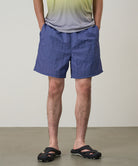 Model wearing navy checkered Gramicci Grid Swim Shorts and a lime and grey gradient t-shirt on a light-tone background.
