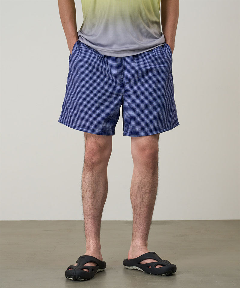 Model wearing navy checkered Gramicci Grid Swim Shorts and a lime and grey gradient t-shirt on a light-tone background.
