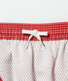 Front view close-up of red and white Gramicci Grid Swim Shorts against a light-tone background.
