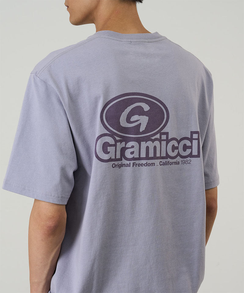 Rear view of a model wearing a light lavender Gramicci '82 Tee on a light tone background.